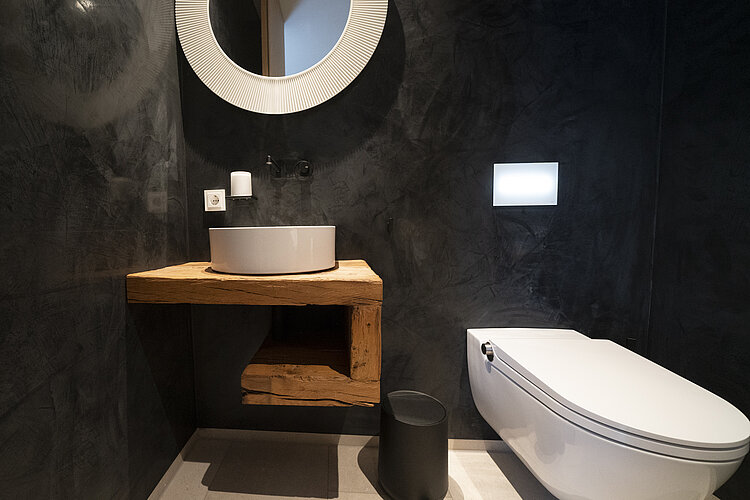 Gäste-WC mit rundem Spiegel, Waschtisch aus Altholz und wandhängendem WC in dunklem Design