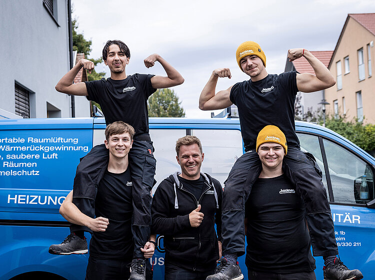 Azubis von Hackner Haustechnik sitzen auf den Schultern ihrer Kollegen, posieren lachend vor Firmenfahrzeug