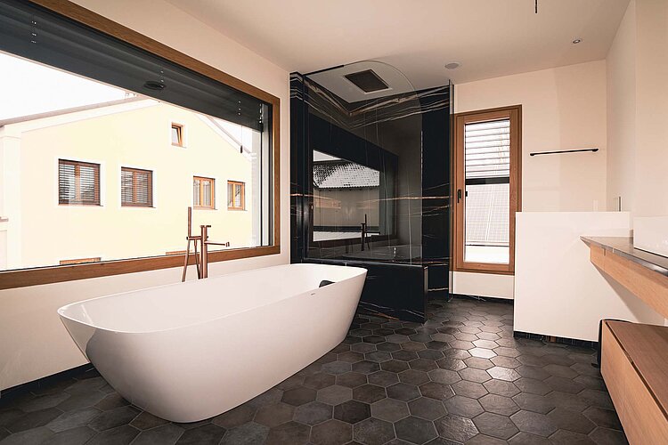 Modernes Badezimmer mit freistehender Badewanne, schwarzem Duschbereich und großen Holzfenstern