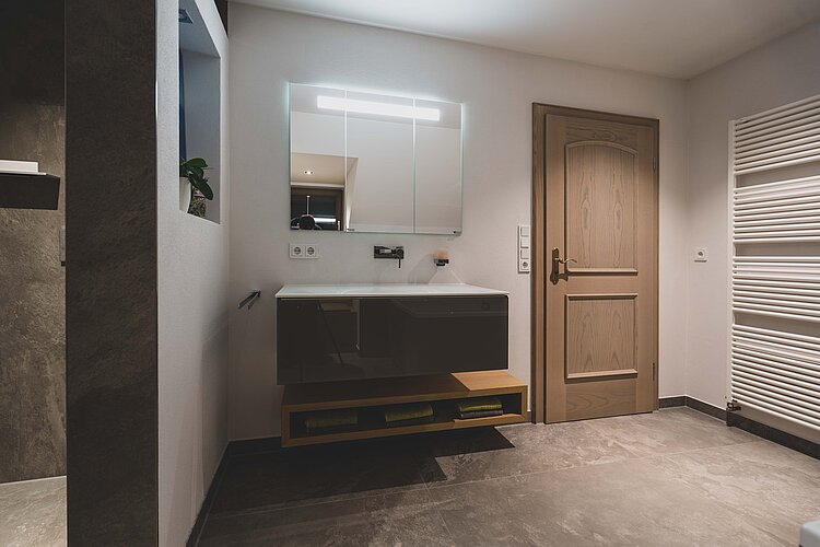 Helles Badezimmer mit großem beleuchtetem Spiegelschrank, Holzdetails und modernem Waschplatz