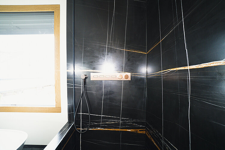 Exklusive Dusche mit schwarzem Marmor, goldenen Linien und edler Bedieneinheit