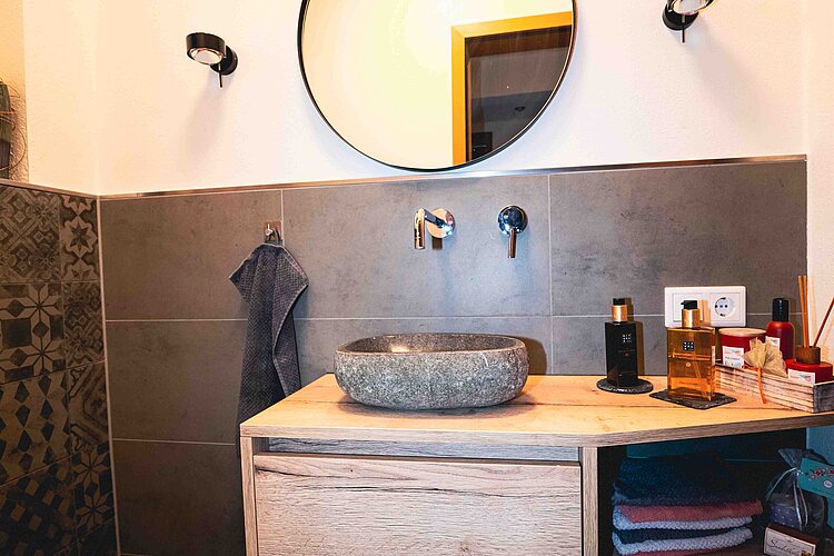Gäste-WC mit rustikalem Natursteinwaschbecken, rundem Spiegel und dekorativen Accessoires