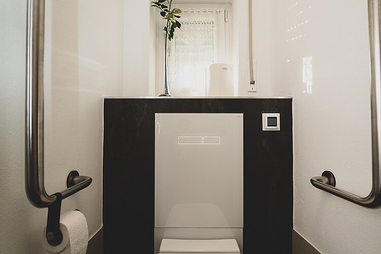 Barrierefreies WC mit seitlichen Edelstahl-Haltegriffen und Fensterbank mit Dekoration