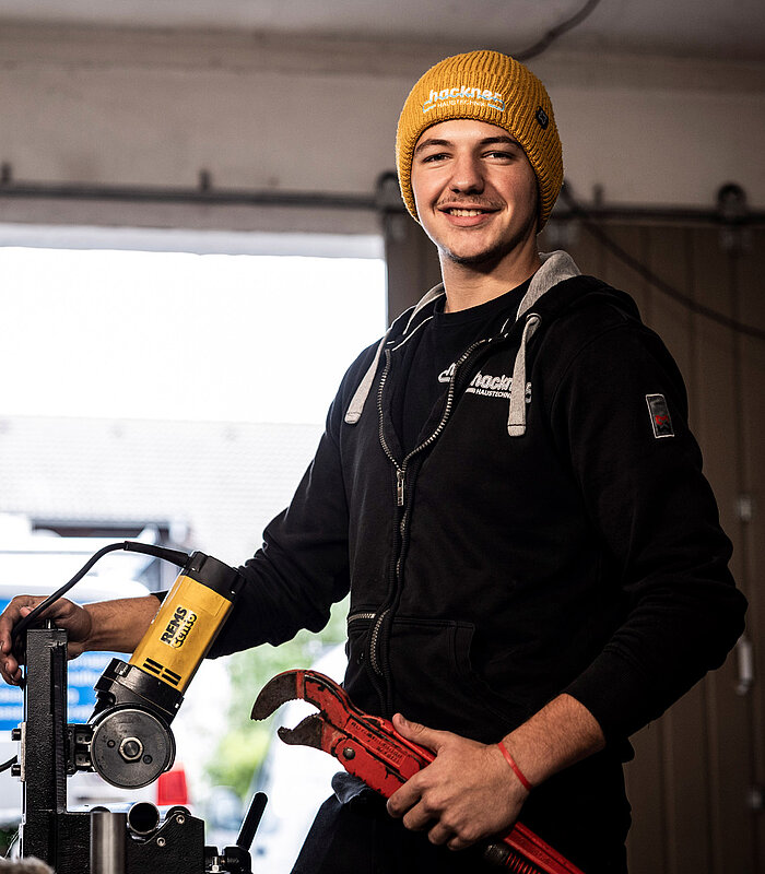 Auszubildender von Hackner Haustechnik mit Mütze, Rohrzange und REMS-Gerät in der Werkstatt