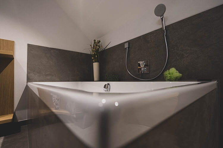Moderne Badewanne unter Dachschräge mit dunkler Wandverkleidung und stilvoller Deko