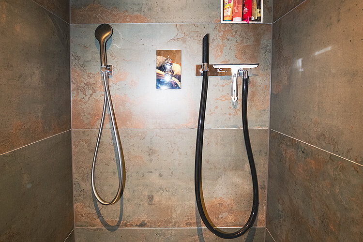 Offene Dusche mit zwei Handbrausen, integrierter Nische und Natursteinoptik