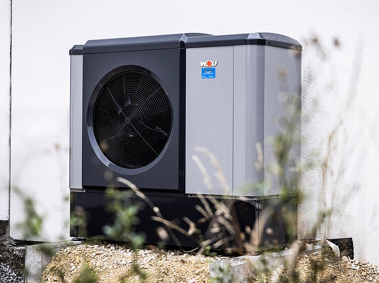 Außenstehende Wärmepumpe von Dimplex an einer Hauswand, montiert auf einem Kiesbett mit Anschlussleitungen.