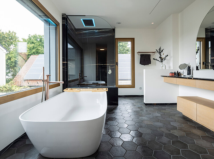 Modernes Badezimmer mit freistehender Badewanne, großer Glasdusche und Blick auf Häuser mit Solaranlagen