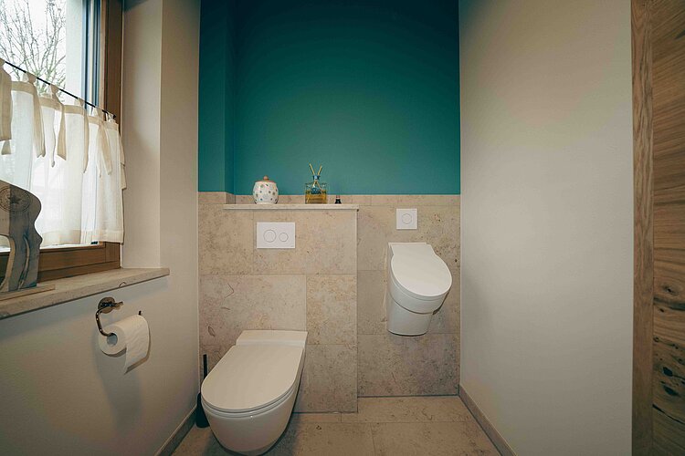 Modernes Badezimmer mit sattgrüner Wand, wandhängender Toilette und Urinal in klarer, reduzierter Gestaltung