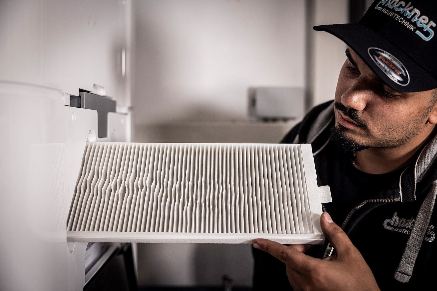 Mitarbeiter von Hackner Haustechnik prüft einen weißen Luftfilter an einem Lüftungsgerät
