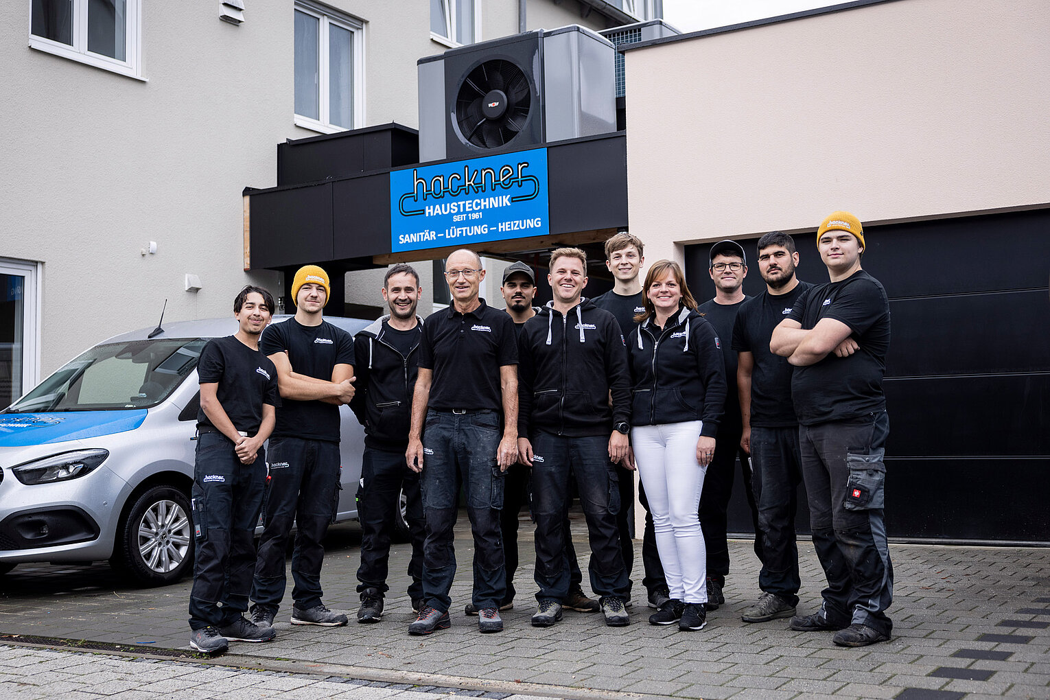 Team von Hackner Haustechnik posiert gemeinsam vor dem Firmengebäude mit Logo und Fahrzeug