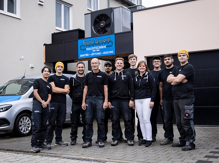 Team von Hackner Haustechnik posiert gemeinsam vor dem Firmengebäude mit Logo und Fahrzeug
